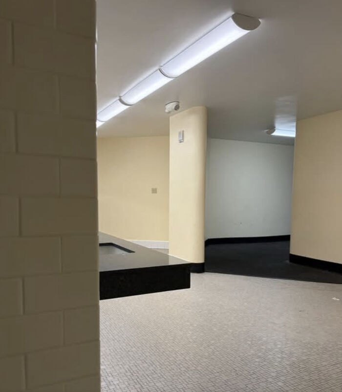 An empty, tiled bathroom with yellow walls and a long counter, a haunting liminal space.