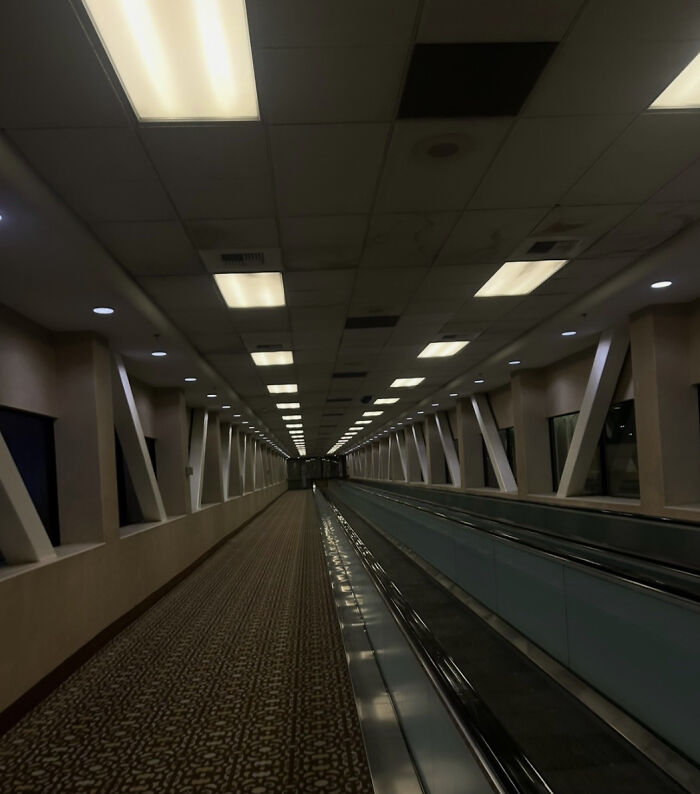 Long, empty airport concourse with a moving walkway and bright overhead lights, a haunting liminal space.