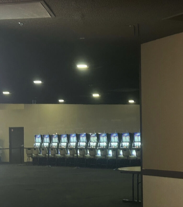 A row of empty slot machines in a dimly lit, haunting liminal space with dark carpets and a low ceiling.