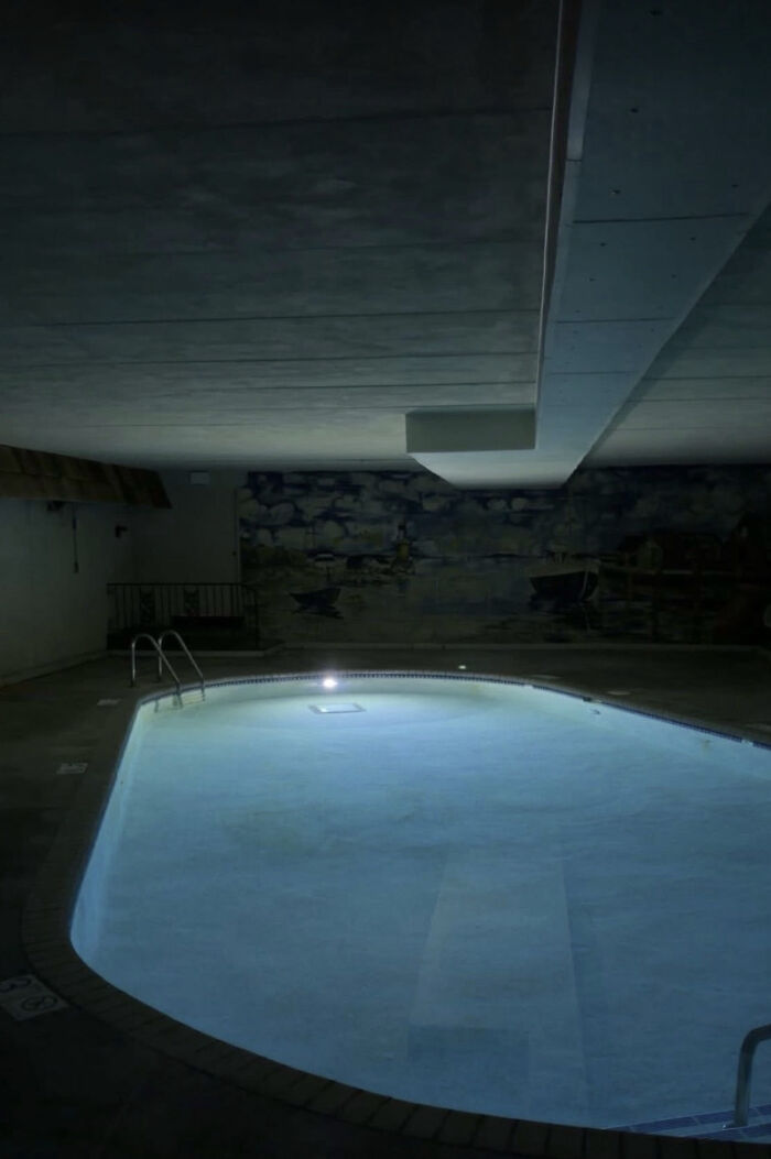 An eerie, dimly lit indoor swimming pool, a haunting liminal space with glowing water and dark surroundings.