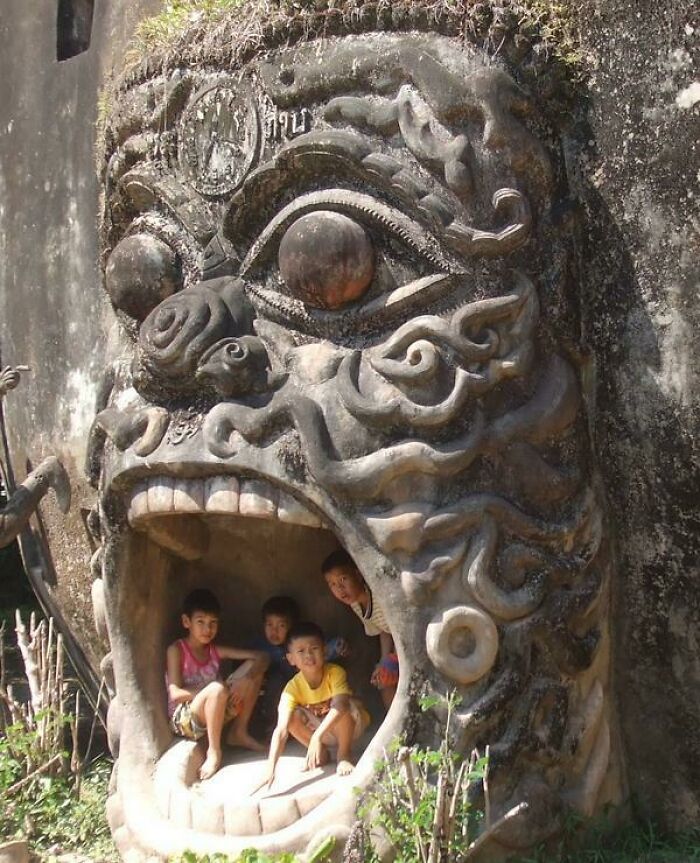 Children sitting inside a large creepy stone sculpture resembling a monstrous face