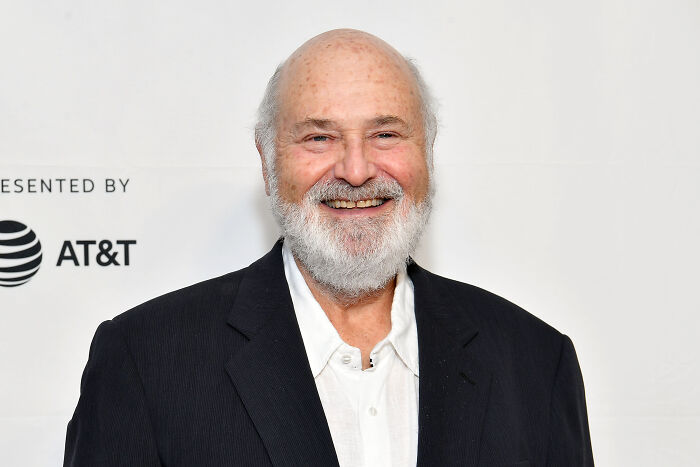 A smiling man with a white beard and bald head, wearing a white shirt and black jacket, in the final season of The Bear.