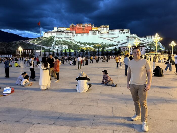 A traveler in China standing in a bustling plaza at dusk, with the illuminated Potala Palace in the background.
