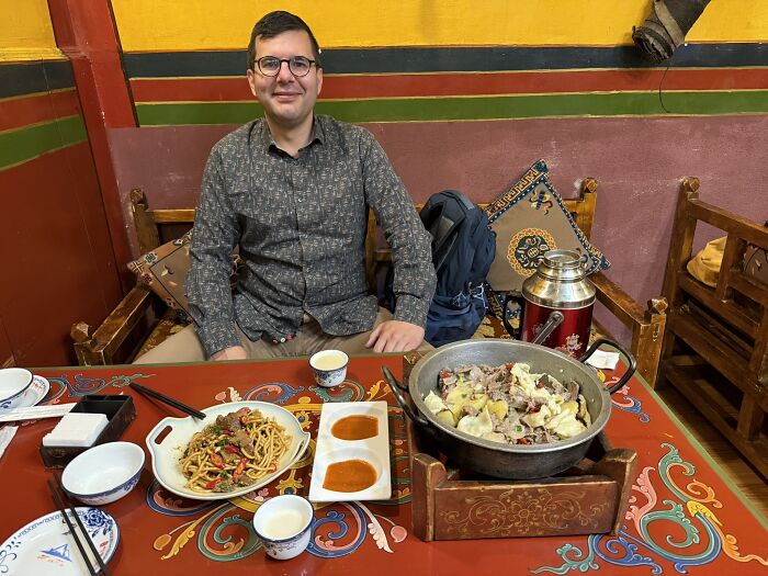 A traveler in China enjoying a traditional meal of noodles and a hot pot, seated at a colorful table in a restaurant.