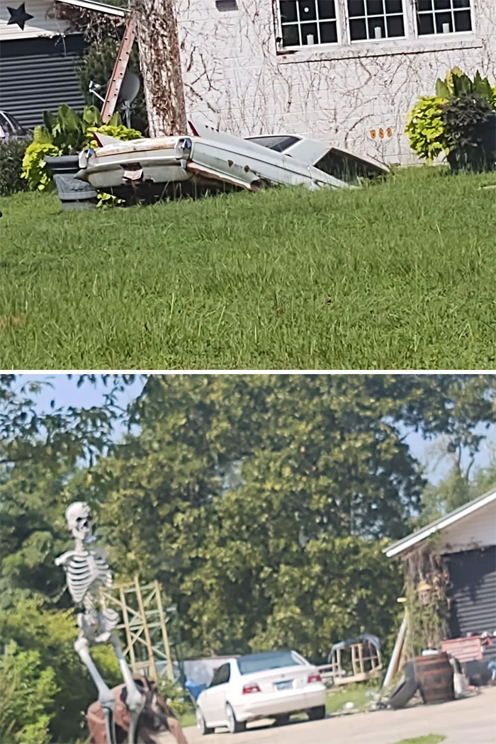 Vintage car partially buried in grass outside house in unusual scene
