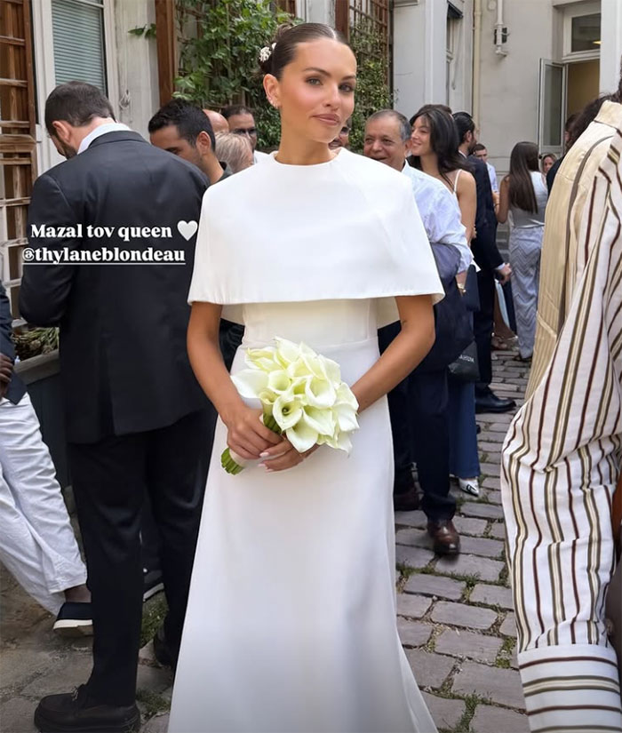 Thylane Blondeau wedding in a white dress, holding a bouquet of white flowers, surrounded by guests.