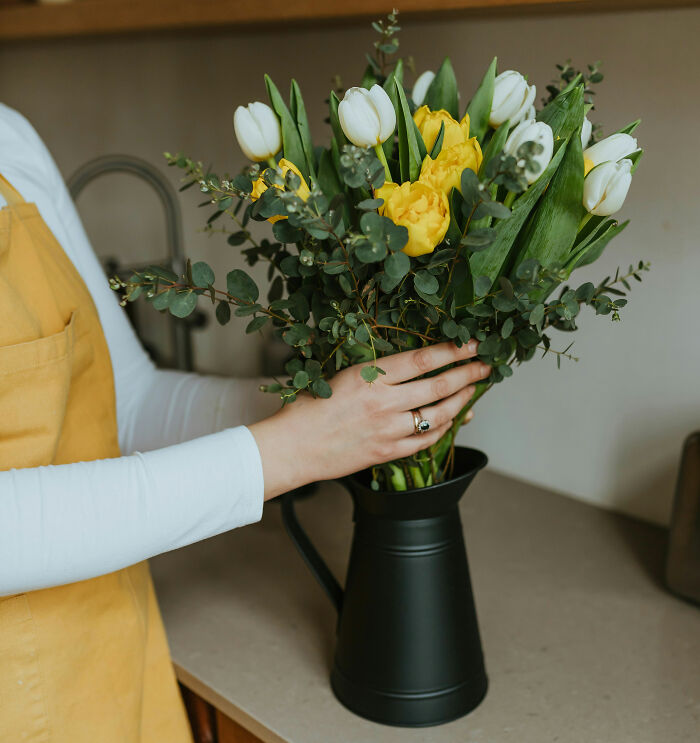 A woman putting a bouquet of white and yellow tulips into a black vase. Women decided to marry their partner.