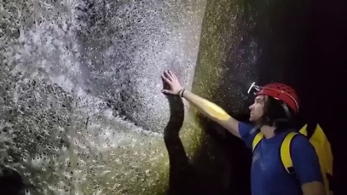 A person in a hard hat with a headlamp touching a dark, textured cave wall; things that should be left alone.