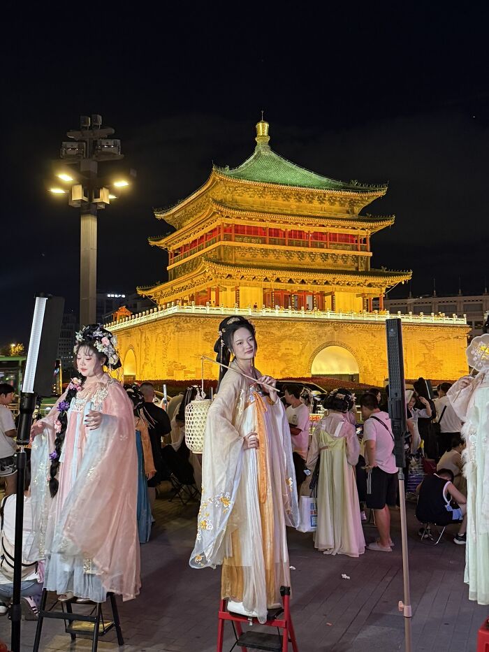 Travelers in traditional attire posing at night in front of an illuminated historical building in China.