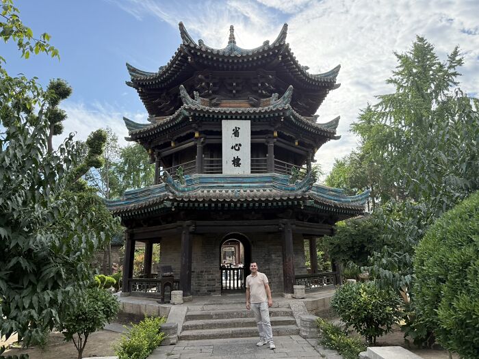 A traveler in China stands before an ancient multi-tiered temple with intricate architectural details and green roofs.