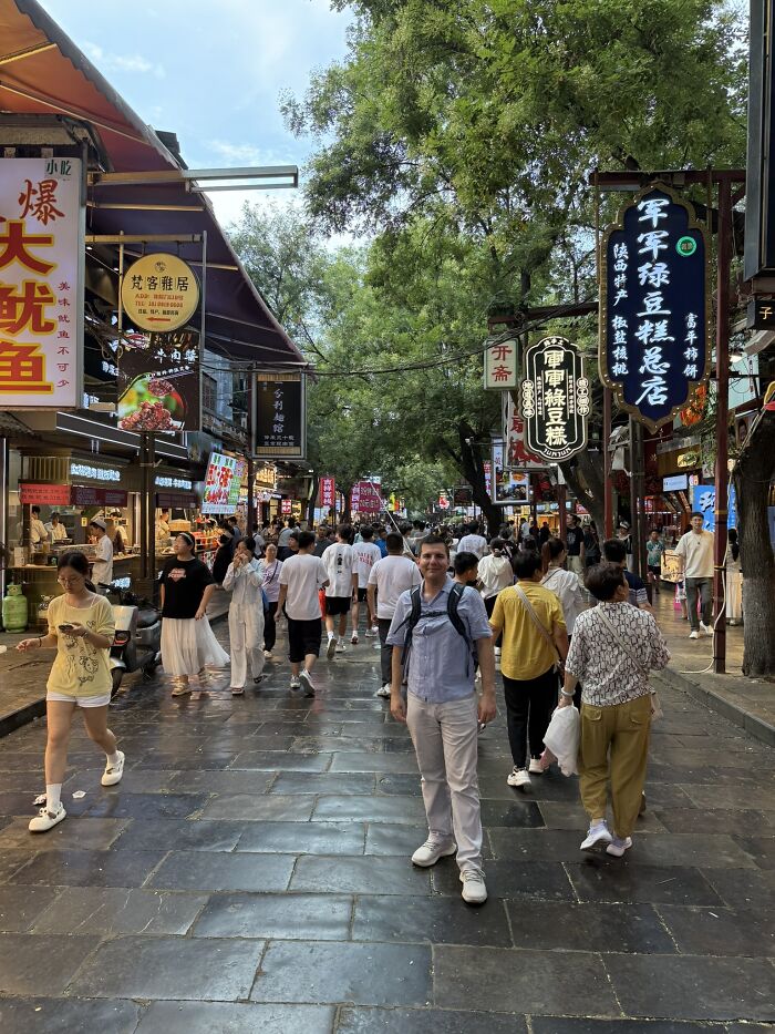 A traveler stands on a bustling street in China, surrounded by locals and colorful market stalls, experiencing local life.