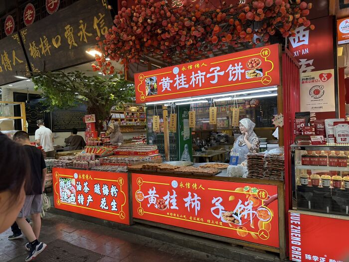 A vibrant street stall in China, adorned with red signs and lights, selling traditional snacks to travelers.