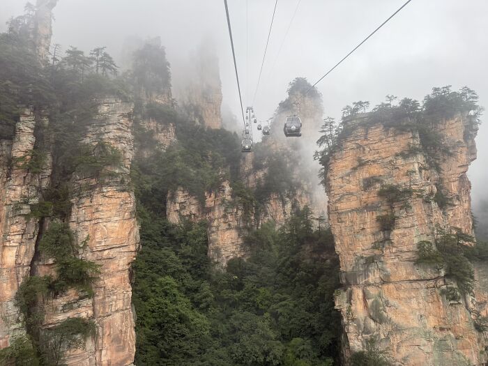 A cable car ascends through the misty, towering rock formations and lush greenery, showcasing the unique China landscape.