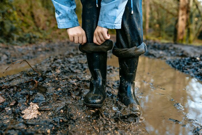 Child adjusting muddy black rubber boots in forest