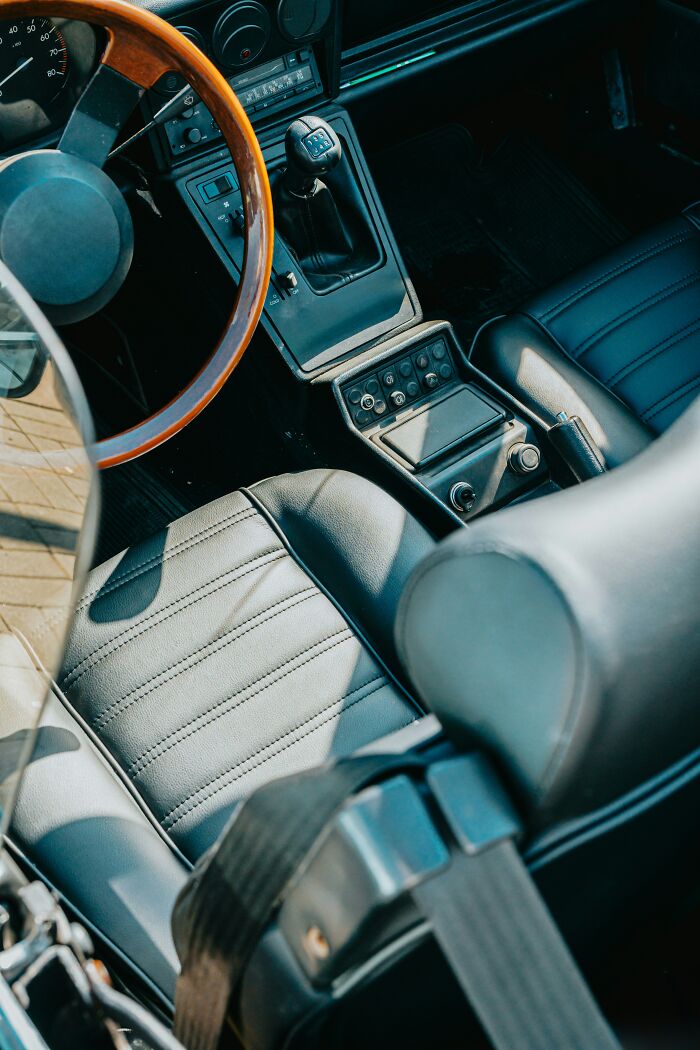 A vintage car interior with a wooden steering wheel and black leather seats, hinting at hidden true selves and secret stories.