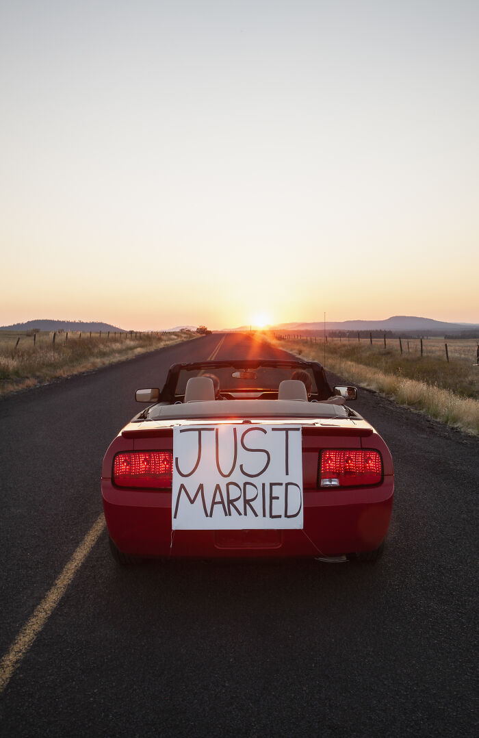 Red convertible with Just Married sign driving into sunset