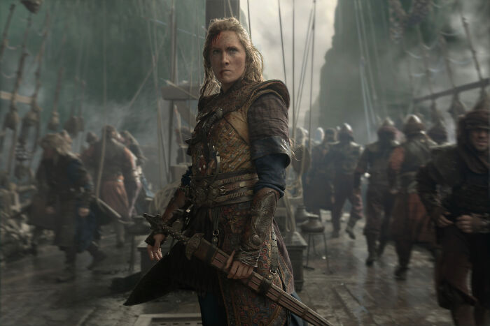 A fierce woman warrior with a sword stands on a ship deck amidst chaos during a brutal naval clash in House of the Dragon. A fierce woman warrior with a sword stands on a ship deck amidst chaos during a brutal naval clash in House of the Dragon.