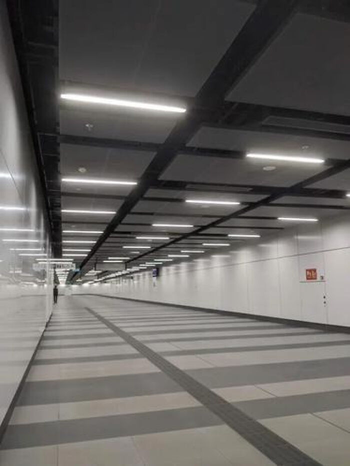 A vast, empty modern underground walkway with bright strip lighting, a classic liminal space.
