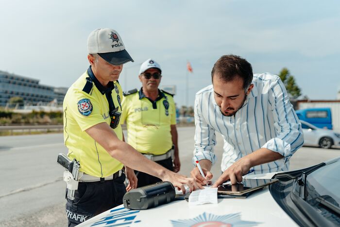 Police officer writing a ticket while a man signs the document on a patrol car