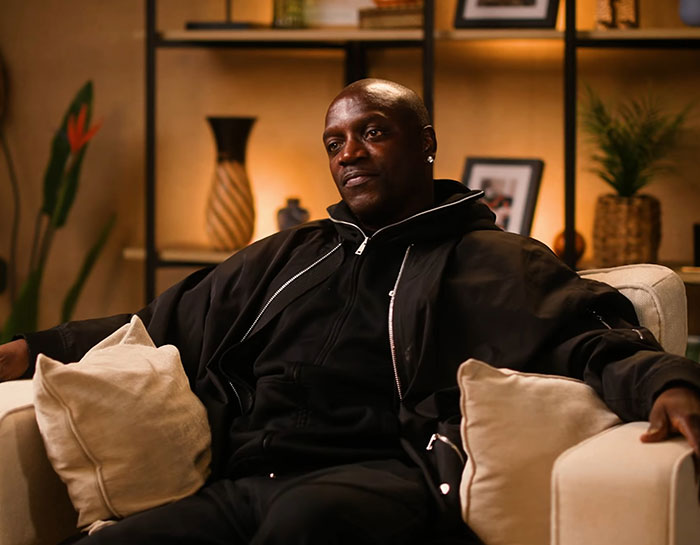 Akon sitting on couch wearing black jacket in interview setting