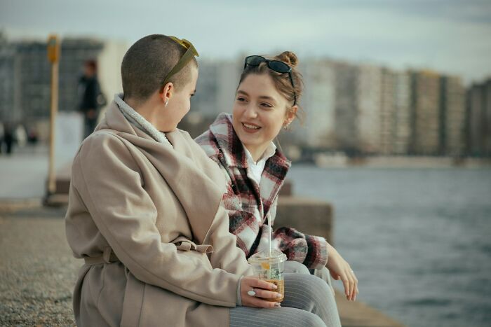 Two friends smiling and talking by waterfront enjoying comforting conversation
