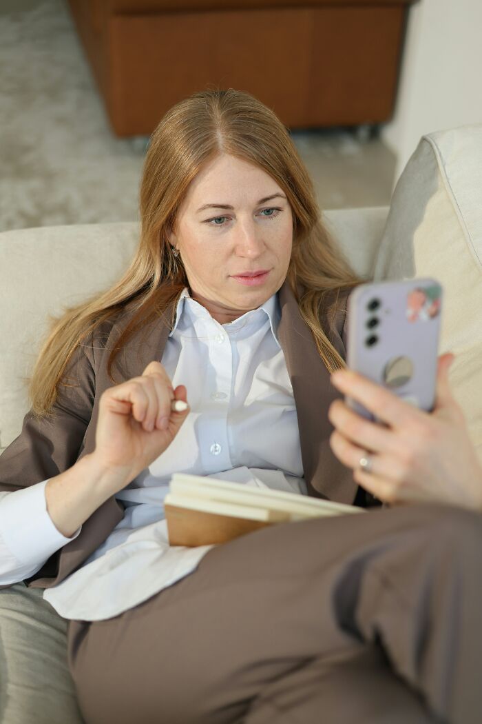 Blonde woman in suit looking at phone while holding notebook