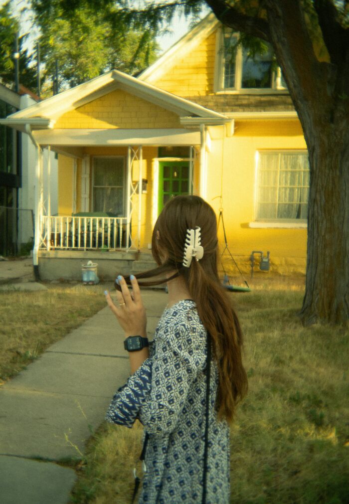 Woman with long hair standing in front of yellow house on sunny day