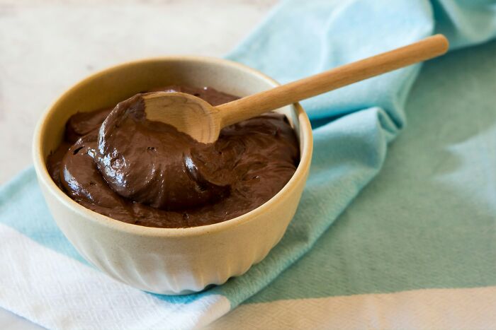 Bowl of chocolate pudding with wooden spoon on blue cloth
