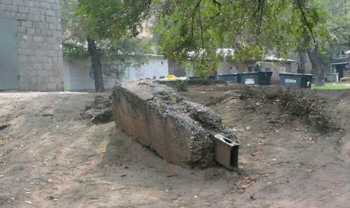 Broken concrete slab partially buried in dirt outdoors with trees
