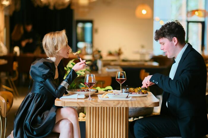 A couple having dinner, the woman showing turn offs while eating at a restaurant.