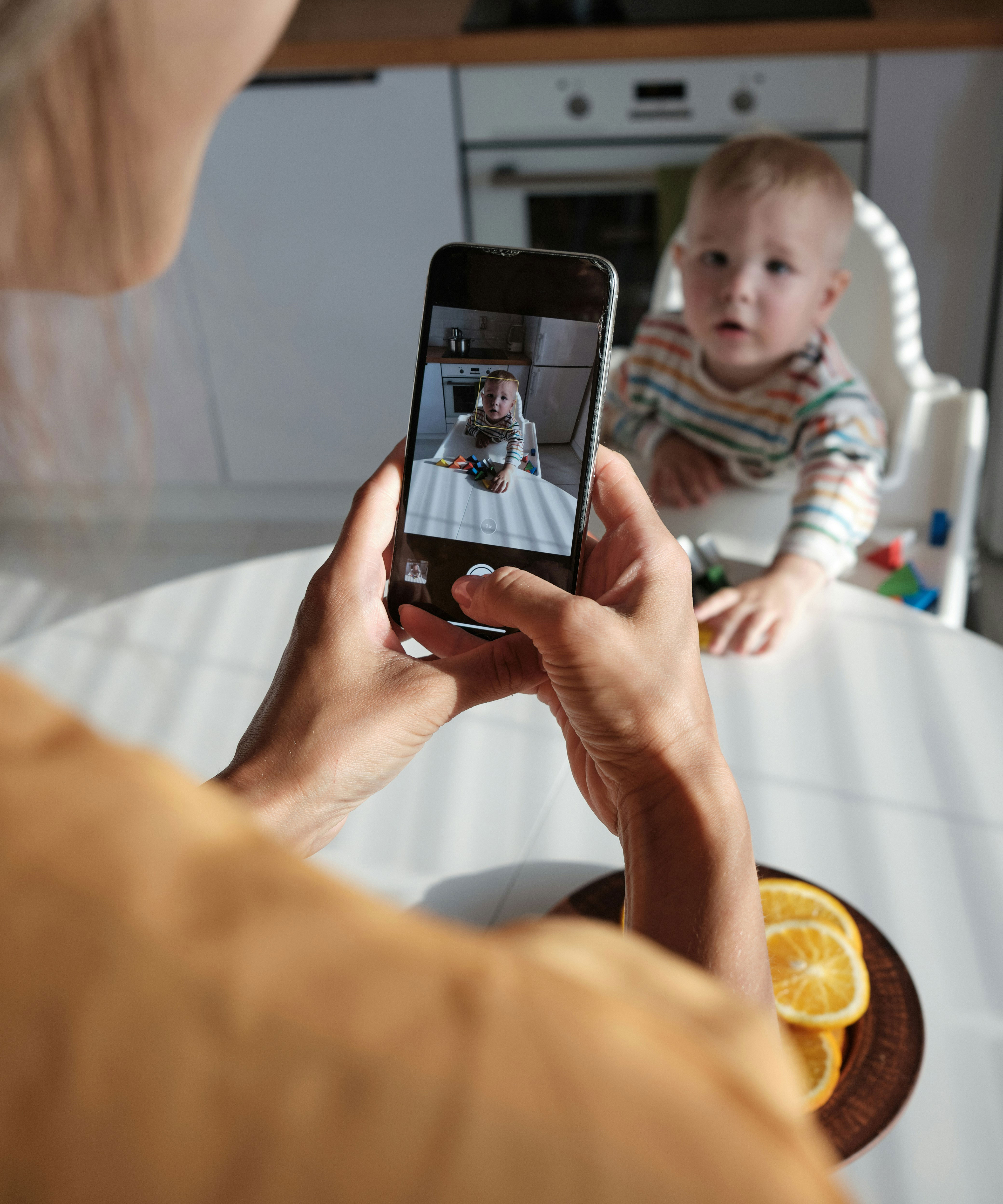 Taking photo of baby in highchair with phone showing baby on screen