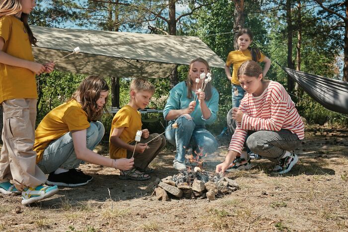 A group of children and adults roasting marshmallows over a campfire, an unusual job experience in outdoor recreation.