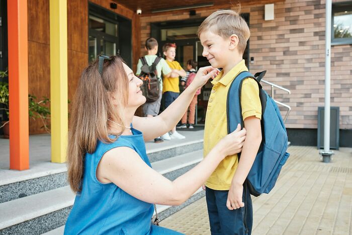 Teacher adjusting young boy's backpack outside school showing Gen Alpha illiteracy concerns