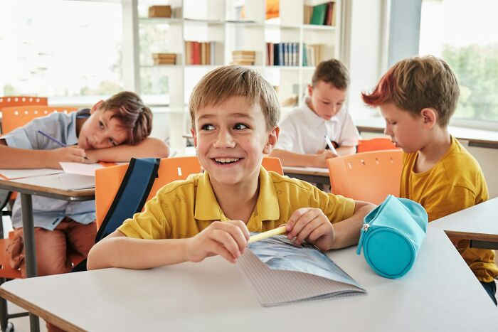 Smiling schoolboy laughing in classroom depicting class clown consequences scenario