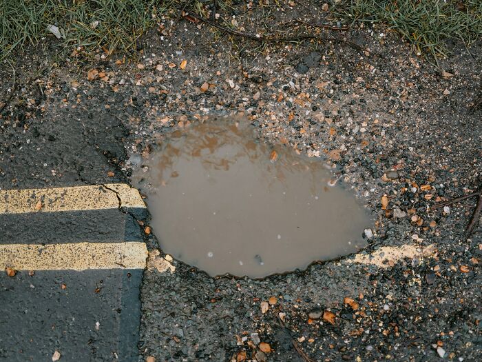 A puddle in a cracked road with double yellow lines, showing a real problem.