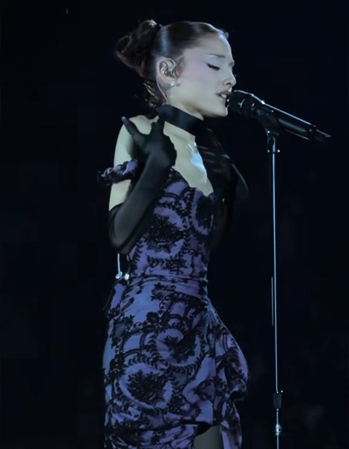 Ariana Grande performing on stage in a purple lace dress during her tour