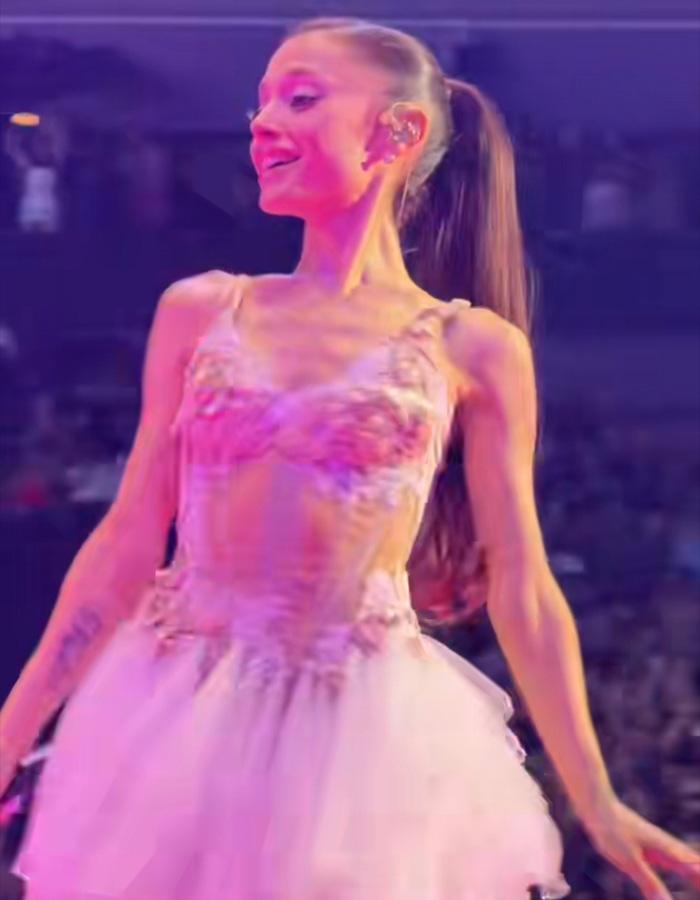 Ariana Grande smiling in a pink floral corset dress during her concert