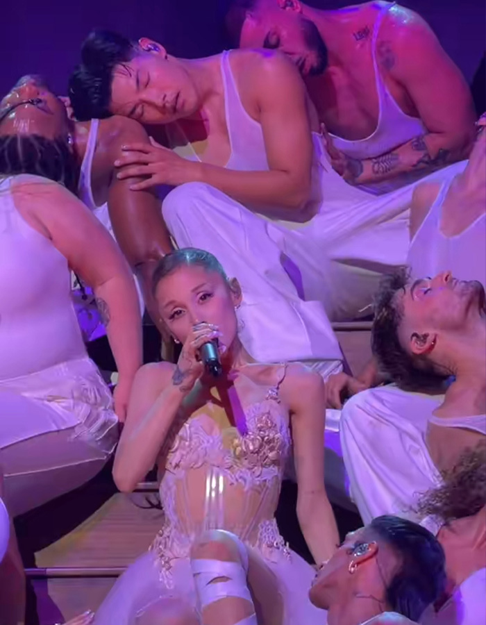 Ariana Grande singing with backup dancers in white outfits on stage