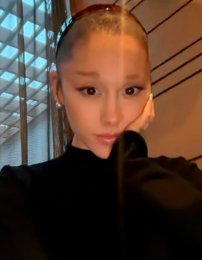 Close-up selfie of Ariana Grande with a hand on her cheek indoors
