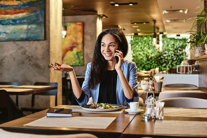 A woman talks on the phone, looking happy, while sitting at a restaurant table. Mom hijacks aunt's birthday plans. A woman talks on the phone, looking happy, while sitting at a restaurant table. Mom hijacks aunt's birthday plans.