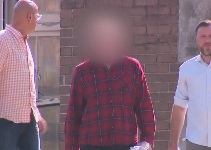 Blurry image of a man in a red plaid shirt walking outside a brick building