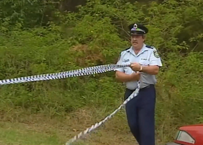 Police officer holding crime scene tape near wooded area