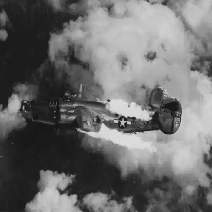 An airplane on fire, trailing smoke, falling through clouds, one of many historical photos.