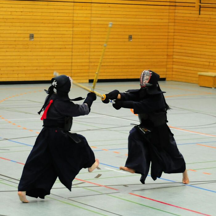 Two kendo practitioners sparring with shinai sticks in gymnasium