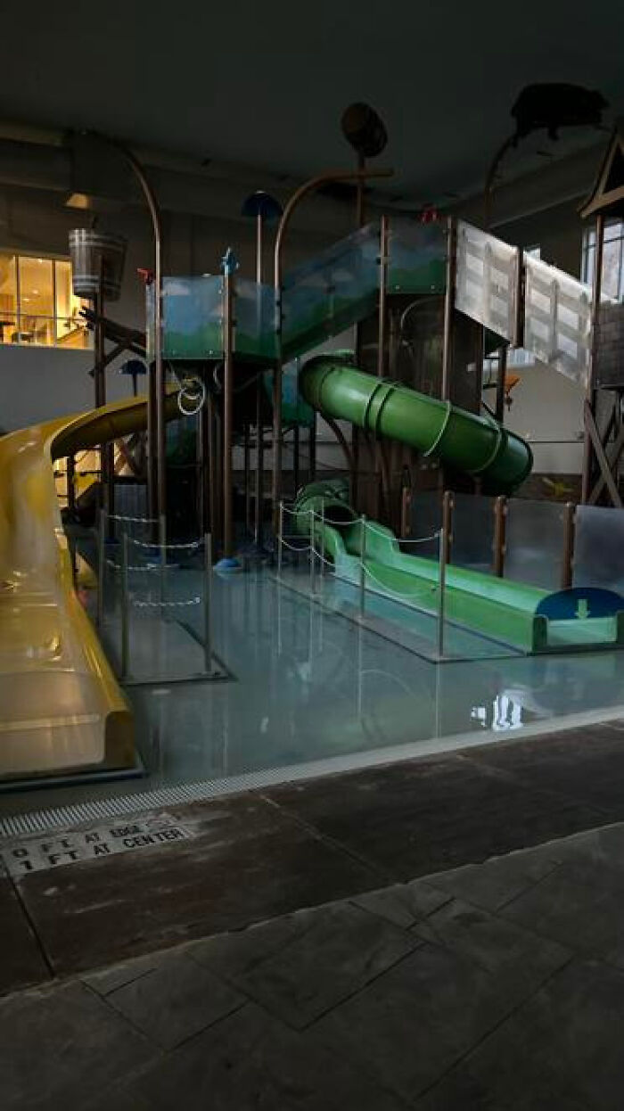 Abandoned indoor water park with slides submerged in still water, a haunting liminal space.