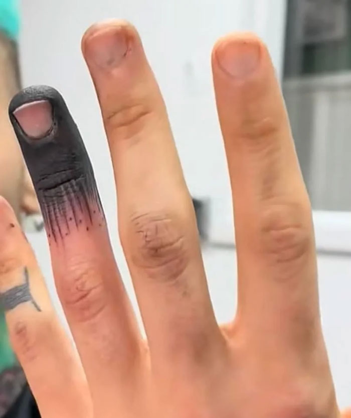 A finger tattooed solid black at the tip, showing a tattoo artist's questionable talent.