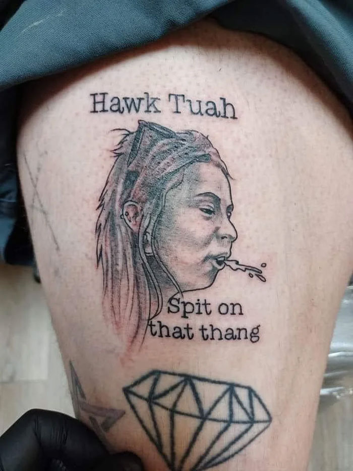 A tattoo on a person's leg showing a woman spitting, with the text 'Hawk Tuah' and 'Spit on that thang'. A questionable tattoo idea.