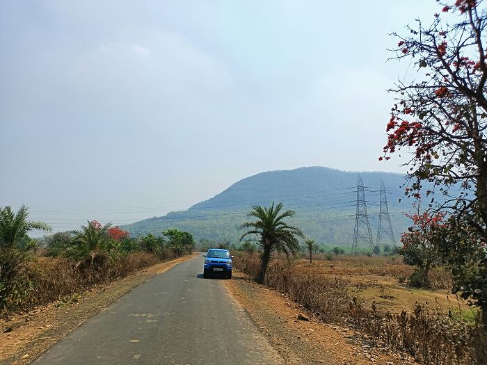 Car driving on a rural road with hills and power lines in the background