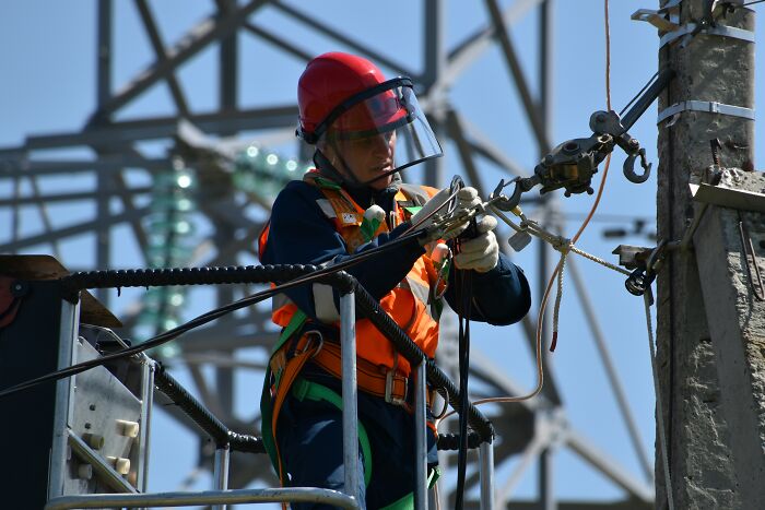 Electrician working on power lines wearing safety gear and helmet