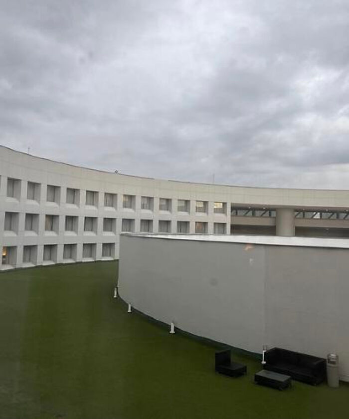 A curved building with many windows and a green rooftop patio, depicting a haunting liminal space.